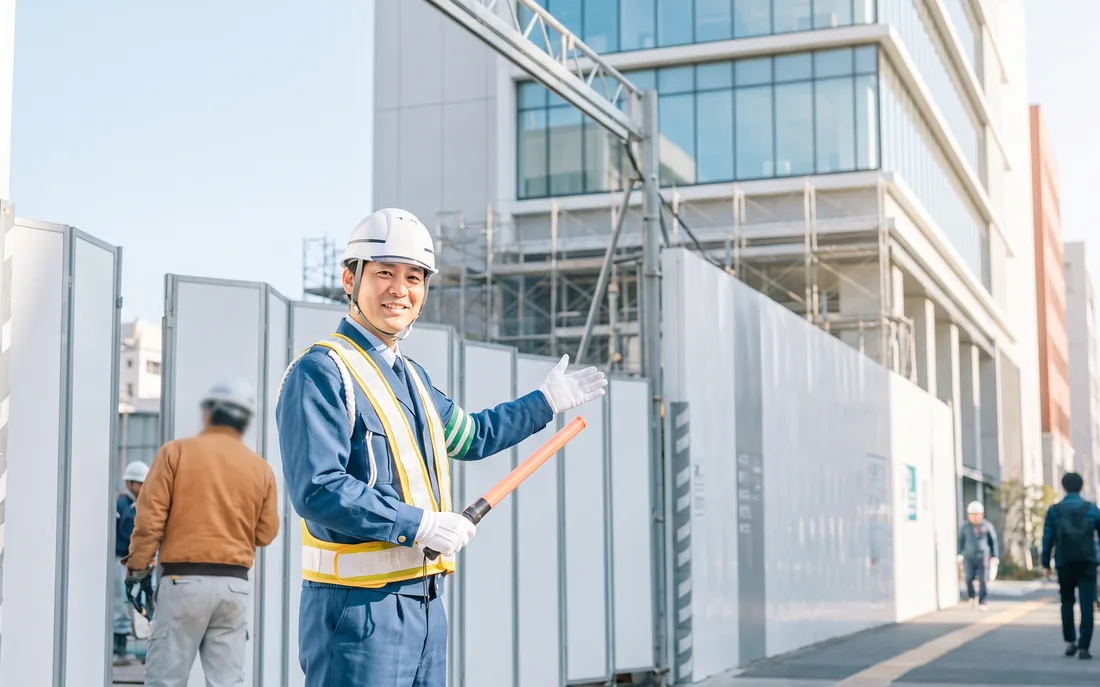 工事現場で誘導灯を持ち交通誘導を行う警備員